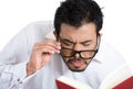 Portrait of a young nerdy guy with eye glasses trying to read book but having difficulties seeing text because of vision problems