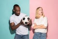 Closeup portrait of young couple, man, woman with football ball. They are serious, concerned on pink and blue background Royalty Free Stock Photo