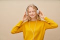 Closeup portrait of young woman closed eyes listening music via headphones on beige wall. Royalty Free Stock Photo