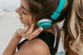 Closeup portrait young woman with long curly hair enjoying lovely music through blue headphones. Walking on seafront Royalty Free Stock Photo