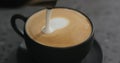 Closeup pouring steamed milk into cappuccino in black cup on terrazzo countertop