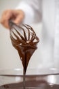 Closeup pouring tasty dark melted chocolate on whisk, white background