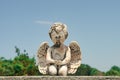 Closeup of praying baby angel statue on tombstone with trees and blue sky behind