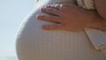 Closeup pregnant female belly at sunlight. Unknown husband hands caressing tummy