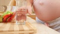 Closeup of pregnant woman with big belly drinkng vitamin pill while having breakfast on kitchen at morning. Concept of