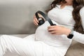 Closeup pregnant woman with headphones on belly, listen music