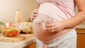 Closeup of pregnant woman holding glass of water and touching big abdomen on kitchen. Concept of healthy lifestyle Royalty Free Stock Photo