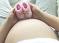 Closeup of pregnant woman holding pink baby booties on her belly Royalty Free Stock Photo