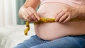 Closeup of pregnant woman sitting on bed and measuring her big belly with measuring tape Royalty Free Stock Photo