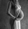 Closeup pregnant woman touching her belly while standing over gray wall background