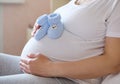 Closeup of pregnant woman waiting for baby, sitting on bed with baby booties on her belly. Happy pregnancy. Anticipation