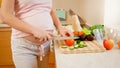 CLoseup of pregnant yougn woman cooking on kitchen and cutting fresh tomato. Concept of healthy lifestyle and nutrition Royalty Free Stock Photo