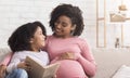 Little black girl and her pregnant mom enjoying reading book together