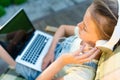 Closeup of pretty teen girl in headphones listening to music using a laptop outside on the terrace in the garden Royalty Free Stock Photo