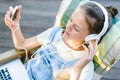 Closeup of pretty teen girl in headphones listening to music using a laptop outside on the terrace in the garden Royalty Free Stock Photo