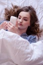 Closeup of pretty teenage girl lying in bed an looking at her mobile phone Royalty Free Stock Photo