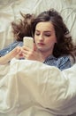 Closeup of pretty teenage girl lying in bed an looking at her mobile phone Royalty Free Stock Photo