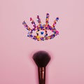 Closeup of professional cosmetic makeup brush with eye shape made of shiny colorful sparkles on pink background with copyspace for
