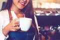 Closeup of professional female barista hand making and holding white cup of coffee. Happy young woman at counter bar in restaurant