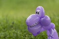 Closeup of purple balloon animal dinosaur in green grass of back