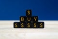 Closeup of a pyramid of black cubes with gold Dollar signs and text buy on them