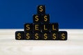 Closeup of a pyramid of black cubes with gold Dollar signs and text sell on them