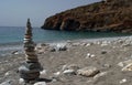 Closeup of pyramid of stones on sandy beach with stones. Blue sea, coastline and rocky mount. Stone symbol