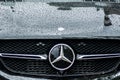 Closeup of rain drops on black Mercedes car front parked in the street