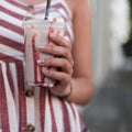 Closeup of raspberry sweet milkshake in the hands of a fashionable young woman. Stylish girl in a striped dress