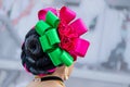 Closeup of rear view of Hispanic dancer`s headress and hairdo in bright pink and green against blurred background