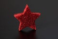 Closeup of a red and glittery star-shaped Christmas ornament, isolated on a dark background. Royalty Free Stock Photo