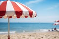 Closeup a red and white striped beach umbrella on a background of a summer beach with sun loungers and blue sea or ocean Royalty Free Stock Photo