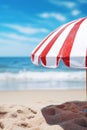 Closeup a red and white striped beach umbrella on a background of a summer beach with sun loungers and blue sea or ocean, vertical Royalty Free Stock Photo