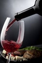 Closeup of red wine pouring into a glass in front of plate with cheese and meat Royalty Free Stock Photo