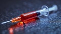 A closeup of a redfilled syringe with an orange cap resting on a reflective dark surface creating a dramatic effect Royalty Free Stock Photo