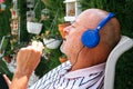 Closeup of a retired senior man listening music with closed eyes in relax time with blue headphones in a garden. Royalty Free Stock Photo