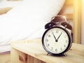 Closeup retro alarm clock on Bedside table with bed background