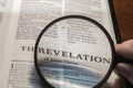 closeup of The Revelation of Jesus Christ from Bible using a magnifying glass to enlarge print.