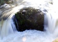 Closeup of a rock dividing a small cascade of water at a river