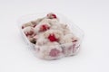 Closeup of rotten moldy raspberry in plastic box on white