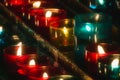 Closeup of rows of candles burning in multicolored glass tealights in a church Selective focus Royalty Free Stock Photo