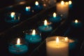 Closeup of rows of prayer candles burning in blue glass tealights in a church