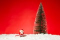 Closeup of a Santa Claus toy on fae snow with a Christmas tree on it against a red background Royalty Free Stock Photo
