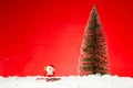 Closeup of a Santa Claus toy on fae snow with a Christmas tree on it against a red background Royalty Free Stock Photo