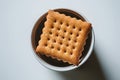 Closeup of a scalloped edge rectangular cracker in a white container on white surface