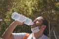 Closeup scene of man with protective mask, drinking water from a disposable plastic bottle, standing in a public park, outdoor. Royalty Free Stock Photo