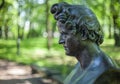 Sculptural bronze antique portrait of a man in profile with curly hair against a blurred background of the park