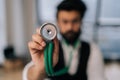 Closeup selective focus of blurred Indian male cardiologist in glasses holding stethoscope on hand for listening check Royalty Free Stock Photo