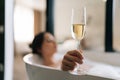 Closeup selective focus shot of young relaxed woman lying in foam bath holding glass champagne enjoying alcoholic drink Royalty Free Stock Photo