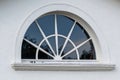 Closeup of a semi circular window with sunburst design on a white wall of a house